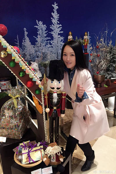 照片中,杨钰莹长发披肩,穿白色收腰风衣,身处充满圣诞氛围的饼屋前