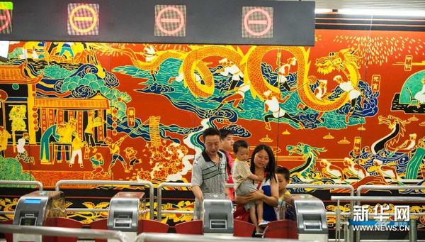 重庆地铁1号线沙坪坝地下车站内，几名乘客通过“民俗风情”壁画前的进站口打卡进站乘车（7月17日摄）。