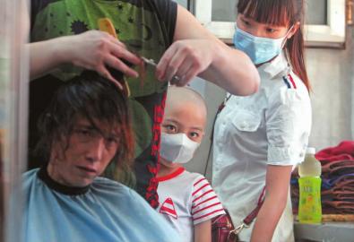 妈妈剪去留了30多年的长发，剃成光头的媛媛和姐姐在一边默默地看着 本报记者 孙立国 摄