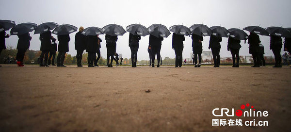 当地时间2014年10月18日,德国柏林,女活动家身穿黑衣,手举雨伞在国会大厦前游行,抗议人口贩卖。图片来源:CFP