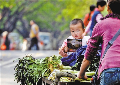 8点40分，渝北区龙溪街道，一卖菜的小贩将孩子放在推车上匆忙地赶路。