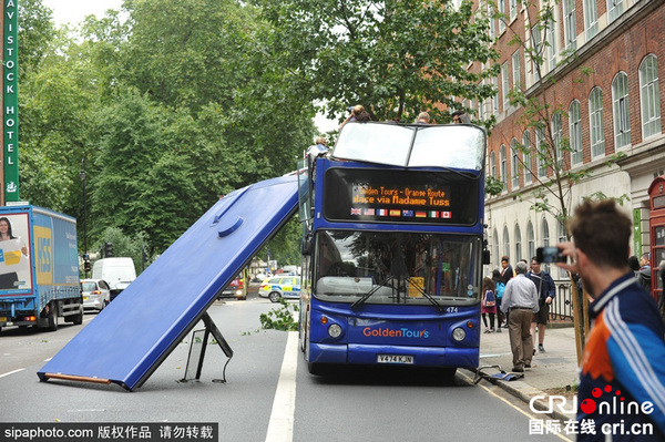当地时间2015年8月3日，英国伦敦，在罗素广场附近的布卢姆茨伯里，一辆旅游巴士车顶整个被树掀翻，造成数人受伤。 图片来源：Sipa Photo