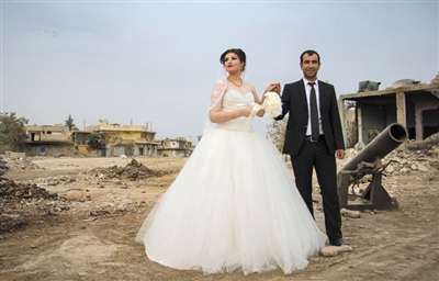 　　近日，在叙利亚城镇科巴尼，一对库尔德夫妻举行婚礼。这是自科巴尼从“伊斯兰国”手中脱离后，首对举行婚礼的夫妻。图片中新郎握着新娘的手走过被战争损坏的建筑。