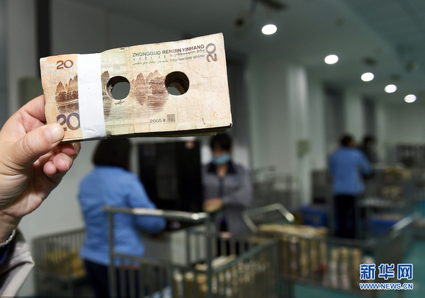 2015年12月3日,四川成都,需要销毁的人民币中心被打孔。随着2015新版百元大钞的发行,旧版的钞票也将慢慢退出流通市场。图片来源:cfp