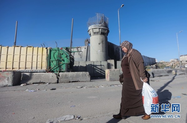 1月6日，拉姆安拉，巴勒斯坦妇女从以军检查站附近隔离墙前走过。巴勒斯坦人要进入耶路撒冷，此处检查站是必经之地。新华网发（法迪·阿奥里摄）