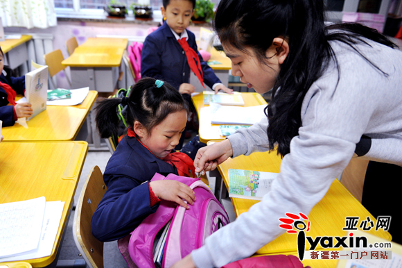 图为乌鲁木齐第十三小学，一名小朋友的书包太厚无法放进桌洞，老师赶紧帮助她处理。首席记者 张万德 摄