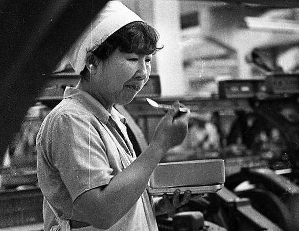 　　在郑州国棉一厂的布机车间内，一位女工在边看机器边吃饭（1990年摄）
