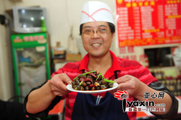 3月30日，乌鲁木齐天山区幸福路眼镜砂锅田螺店，老板向先平端着一盘田螺。图/记者 谢鹏 摄