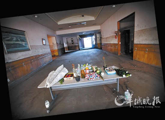 　　宽敞的过道中央放着一张桌子，上面摆满了鲜花、香烛、千纸鹤和饮料瓶，供养逝去的生灵
