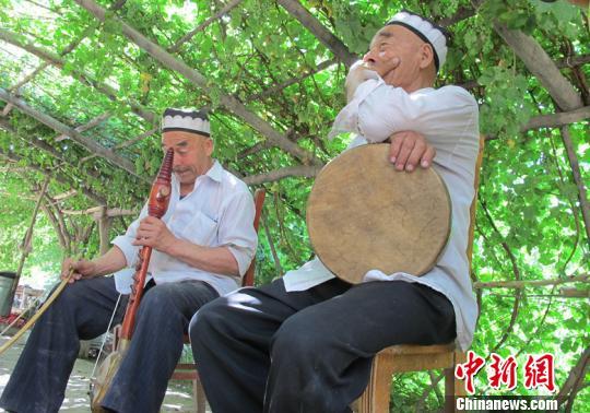 两位老人在院子里的葡萄架下弹唱刀郎木卡姆。　杨喆　摄