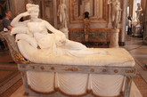 博尔盖塞博物馆（Borghese Gallery）是罗马馆藏最丰富的博物馆之一，正如博尔盖赛博物馆馆长所说他们的收藏品只收藏世界顶级艺术品，二流作品绝对不在馆藏考虑范围内。博尔盖塞博物馆馆藏包括：贝尼尼的多件雕塑；达芬奇、拉斐尔、提香、波提切利和卡拉瓦乔、鲁本斯等多位世界艺术大师代表作品。博尔盖塞家族成员之一卡米洛（Camillo Borghese）在1803年成为拿破仑妹妹波利娜.波拿巴（Pauline Bonaparte）的第二任丈夫，并获得了拿破仑授予的法国王子、帝国卫队总司令等头衔，交换条件是拿破仑从博尔盖塞家族的收藏品为法国政府购买344件艺术珍品，现在这些价值连城的文物都成了卢浮宫的重要藏品。博尔盖赛博物馆内中国人熟悉的艺术家有：贝尔尼尼、卡诺瓦、拉斐尔、提香卡拉瓦乔。《波利娜.波拿巴》（Pauline Bonaparte 1780-1825年）是安东尼奥.卡诺瓦（Antonio Canova 1757-1822年）的作品。这尊半裸的、与真人大小一致的雕像是卡诺瓦在1805-1808年间以拿破仑（Napoleon Bonaparte 1769-1821年）最喜欢的妹妹波利娜为原型塑造的。女主人右手支撑着头，左手拿着象征爱神阿佛洛狄特（Aphrodite 希腊神话，罗马神话中叫维纳斯 Venus）在与天后赫拉（Hera）、智慧女神雅典娜（Athena）的选美比赛中获胜的金苹果，所以这个雕像的另一个名字也叫《作为胜利者维纳斯的波利娜.波拿巴》（Pauline Bonaparte as Venus Victrix）。当时裸体或半裸体的人物肖像还不普遍，所以有些专家怀疑雕像只有头部是以本人为蓝本塑造的，其他部分为替身，毕竟波利娜不是一般人物。波利娜是个极为风流的女子，婚前因与拿破仑手下的一名将军闹出绯闻，被拿破仑逼着两人成婚。她丈夫在30岁时因感染黄热病死去，不久她又嫁给了博尔盖塞家族的一名成员，因风流习性不改，经常与级别很低的士兵和军官有染，丈夫与她分居达十年之久，后被报丈夫在外也有一个情妇。丈夫说波利娜有很多变态的想法和做法，如让高大的非洲男仆背着她去洗澡，将侍女作为脚凳使用等等。1825年在教皇的劝说下丈夫又重新“接纳”了她，三个月后她患癌症去世。在她的婚姻中，当哥哥的拿破仑也得到了不少好处，譬如他迫使博尔盖塞家族从他们的收藏品中以极低的价格卖给卢浮宫或法国政府344件绘画和雕塑珍品，这些拿破仑的“战利品”至今仍挂在卢浮宫的展室里向后人炫耀。