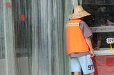 7月16日， 浙江省金华市区，一环卫工人在商场门口“蹭凉”，却不敢走进去享受空调带来的凉爽。