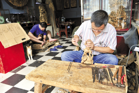 潮州老市区中山路上，郑文雄和父亲郑庆明在自家的店面里精雕细琢着木雕物件，他们店面所在的老街上，专做游客生意的三轮车不时经过