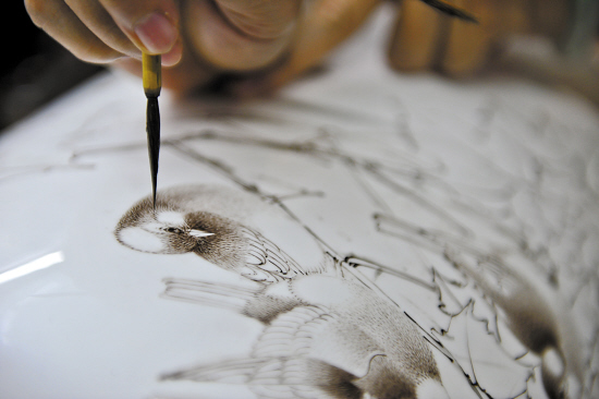 广东省工艺美术大师吴淑云，在瓷白的花樽上精细地勾画着花鸟画。潮州不单制作陶瓷出名，与陶瓷相关的潮州彩绘也出了名师