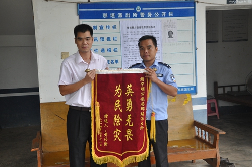 黄兴隆将一面绣着"英勇无畏 为民除灾"的锦旗递到救命恩人李剑民警手